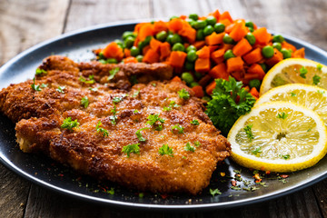 Schnitzel with boiled carrot and peas on wooden background