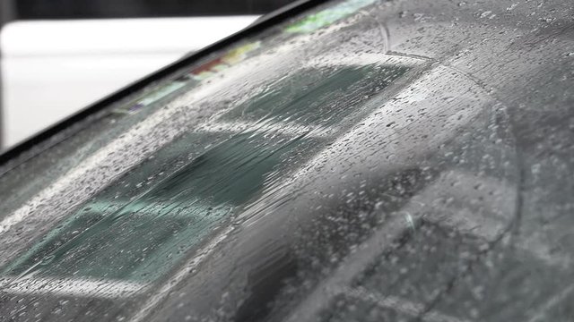 In a rainy day at day time, there are water droplets drop on the windshield on a car