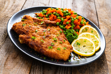 Schnitzel with boiled carrot and peas on wooden background