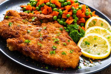 Schnitzel with boiled carrot and peas on wooden background