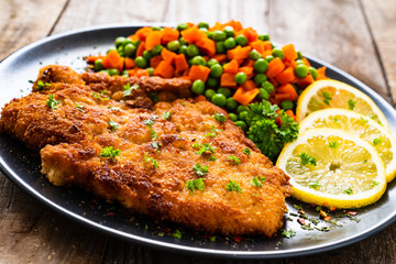 Schnitzel with boiled carrot and peas on wooden background