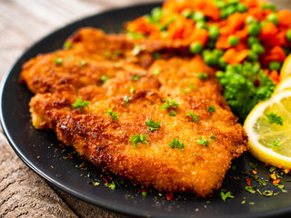 Schnitzel with boiled carrot and peas on wooden background