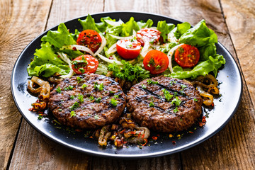 Barbecue steaks with vegetables on wooden background
