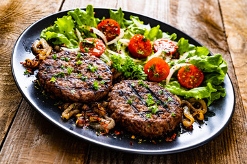 Barbecue steaks with vegetables on wooden background