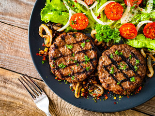 Barbecue steaks with vegetables on wooden background