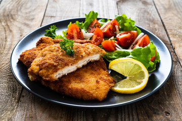 Pork chops with lemon and vegetable salad on wooden background