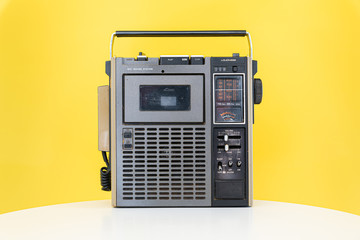 Dirty old 1970s style cassette player radio against a yellow background.