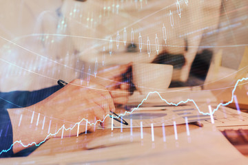 Double exposure of man's hands writing notes of stock market with forex graph.