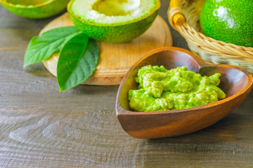avocado puree and avocado halves close -up. avocado puree in a wooden bowl close- up on the table and green ripe avocados.