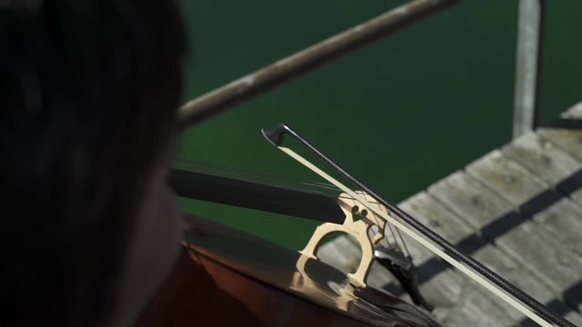 Close up shot of female cello player hands playing cello with cello bow on pier on the lake.