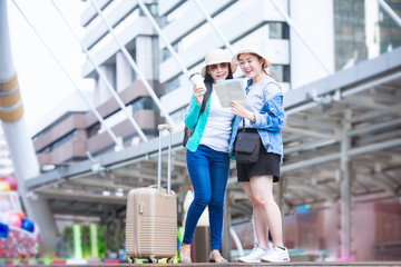 Viewing map. Two young female tourists stand in the street. Two happy tourists holding a map and bag enjoying vacations standing on the city.