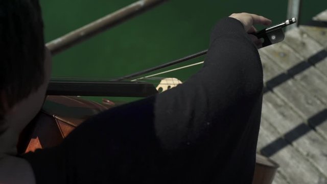 Close up shot of female cello player hands playing cello with cello bow on pier on the lake.