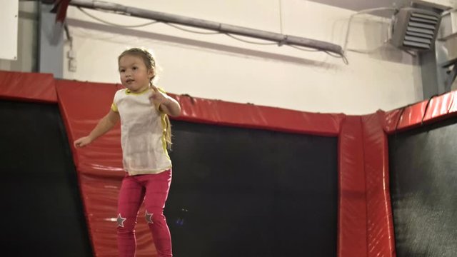 Little girl with pigtails jumps on a trampoline. The child has a serious facial expression.