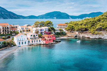 Fototapeta na wymiar Holiday vacation on Kefalonia, Greece. Blue sea bay in front of Assos village. Beautiful view to vivid colorful houses near blue turquoise colored transparent bay lagoon
