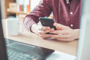 Home office concept: Man is typing on his black mobile phone
