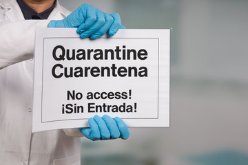 Doctor's hand in medical gloves showing English and Spanish quarantine sign in front of a...