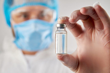 Doctor's hand holding a vial of clear liquid for injection. Close up transparent bottle ampulas...