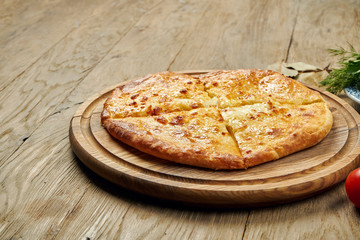 Close up view on tasty traditional Khachapuri - closed baked pie stuffed with melted salt cheese (suluguni) or meat on wooden tray. Traditional georgian food