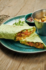 Appetizing shawarma roll with meat, salad and homemade sauce in thin pita bread in blue plate isolated in grey background. Eastern cuisine. Sliced kebab with grilled meat.