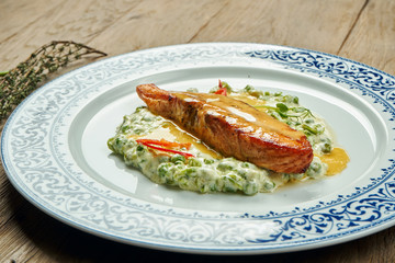 Delicious grilled salmon steak filet with peas in a creamy sauce in a white plate on a wooden background. Tasty seafood