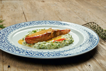 Delicious grilled salmon steak filet with peas in a creamy sauce in a white plate on a wooden background. Tasty seafood