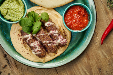 Appetizing rolls of Lyulya kebab - cooked over a lamb minced meat with a side dish of hummus with pita and salsa on ceramic plate. Vertical, wooden background, Eastern cuisine