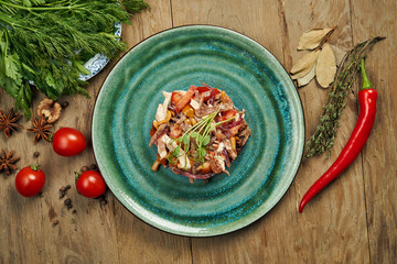 Salad with tomatoes, canned mushrooms, onions and boiled beef on a blue plate on a wooden background. Slavic salad medina. Close up