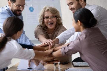 Excited diverse colleagues stack hands in pile motivated for shared victory or win, overjoyed multiracial businesspeople engaged in teambuilding activity at office meeting together, teamwork concept