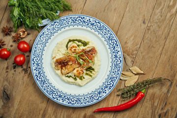 Fried perch fillet with mashed cauliflower in a white plate on a wooden background. Delicious seafood with garnish