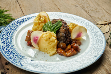 Delicious veal (beef) cheeks with honey sauce and mashed potato garnish in a blue plate on a wooden background. Close up view