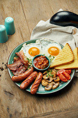 Classic English breakfast: toasts, smoked sausages, bacon, fried eggs, beans and fried toasts on a blue plate. Top view, horizontal. Wooden background