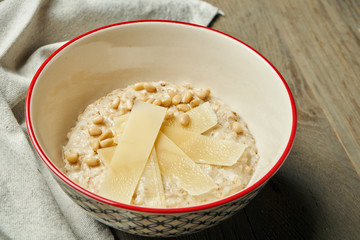 Appetizing and healthy breakfast - oatmeal with parmesan cheese in a bowl on a wooden background. Close up. Copy space