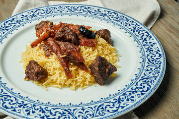 Light, diet pilaf with beef and carrots on a white plate on a wooden background. Top view with copy space for text. Traditional oriental cuisine