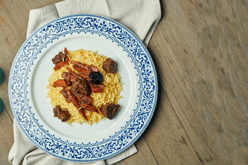 Light, diet pilaf with beef and carrots on a white plate on a wooden background. Top view with copy space for text. Traditional oriental cuisine