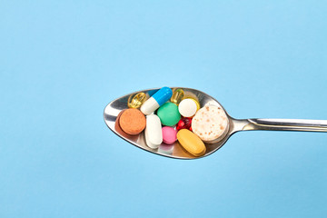 Steel spoon full of various pills. Isolated on blue background.