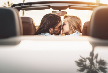 Happy couple kissing in convertible car - Romantic people having tender moment during road trip in...