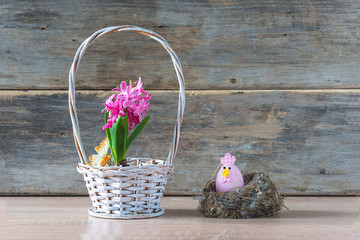 Easter holiday composition. Easter egg in the bird nest and purple hyacinth in wicker basket on old non paint wooden background