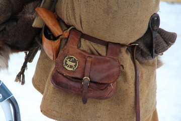 Medieval leather historical waist bag with a copper plaque in the shape of a reindeer hangs on a mans belt in medieval clothes with an ax behind his belt