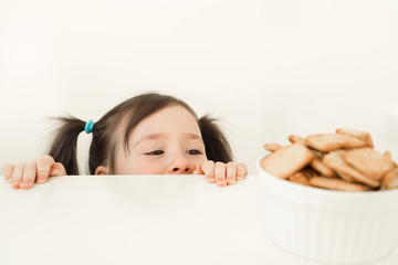 A child spying on cookies. Baby wants to steal sweets. Girl peeks out from the table