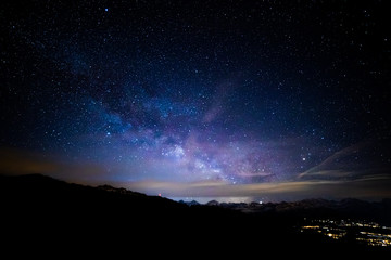 The Milky Way above the city and the mountaints with a cloudy stripe at the horizon