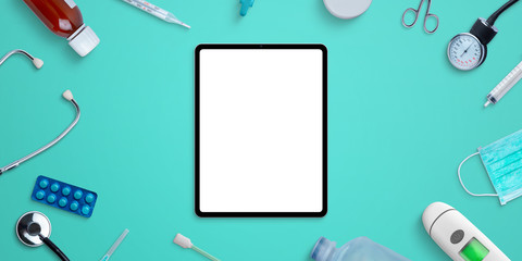 Tablet mockup on hospital desk surrounded by medical equipment and medicines. Top view, flat lay composition