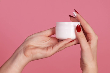 Women's hands hold a jar of cream, pink background