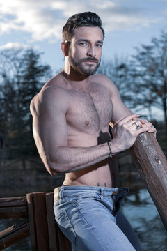 Joven con un tronco de madera. Trabajo en el campo desnudo con el pecho y el abdomen definido del gym tipo firtness. pantal&oacute;n de mezclilla frente al lago en verano con una iluminaci&oacute;n perfecta.