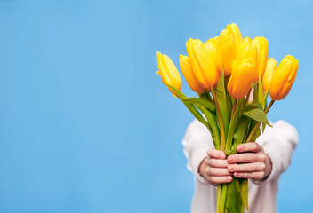 The little boy on a blue background holds in his hands a bouquet of beautiful yellow tulips. The concept of the holiday is March 8, International Women's Day, Mother's Day. Banner, place for text. © Olga Mandrik