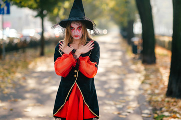 A young witch stands in the street with her arms folded on her chest