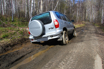 Plakat a grey SUV is towed by a hand winch out of the mud on a forest road