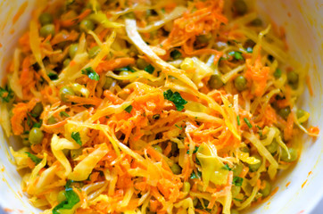 Closeup of a vegetable salad of cabbage, carrots, green peas in a white bowl. Selective focus.