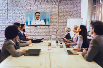 Team of business people looking doctor speech at projector screen in video conference