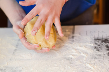 Female hands knead the dough for a sweet cake on a table sprinkled with flour. Making shortcrust pastry at home in the kitchen. Selective focus.