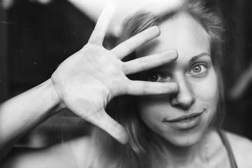 Black and white picture of handsome young girl with fair hair behind glass and covers her face with the hand vand say to stop